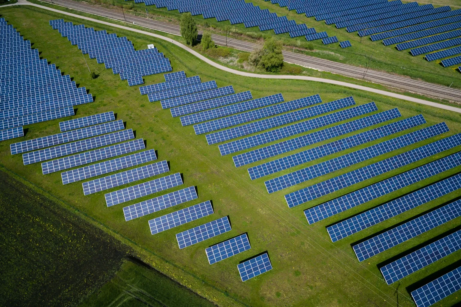 [Image: Partnership — aerial solar farm merging into green farmland, golden hour]